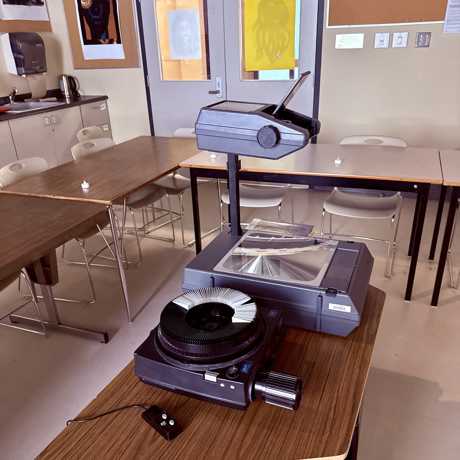 A Kodak carousel slide projector and an overhead projector set up on classroom tables.